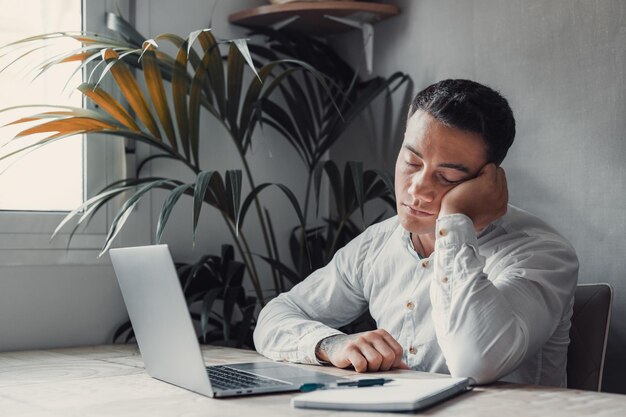 Exhausto joven empleado masculino caucásico escritorio de sueño en la oficina trabajo excesivo preparando un informe