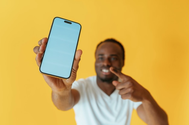Exibição vazia de smartphone segurando homem preto está no estúdio contra fundo amarelo