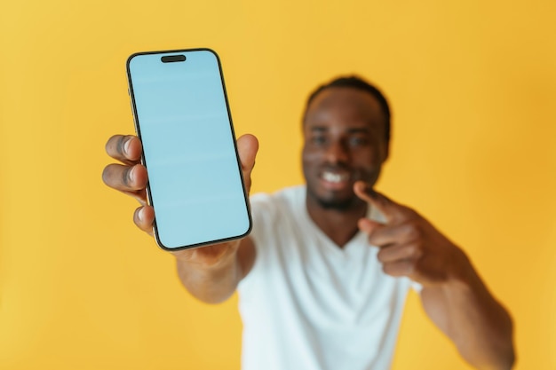 Exibição vazia de smartphone segurando homem preto está no estúdio contra fundo amarelo