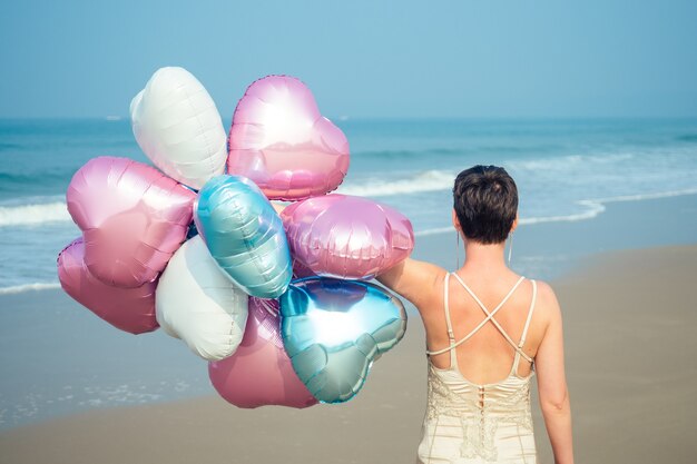 Existe una mujer joven y feliz con el pelo corto sosteniendo un globo aerostático más brillante y brillante. bolas brillantes en manos de una niña descansando en la playa.