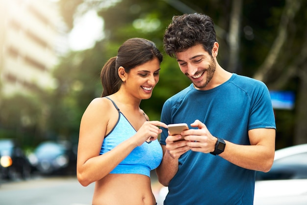 Existem aplicativos para acompanhar sua rotina de exercícios foto de um jovem casal esportivo usando um celular enquanto se exercita ao ar livre