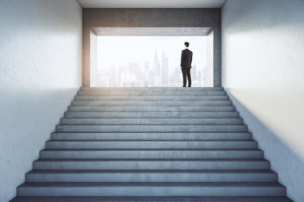 Foto el éxito empresarial con vista hacia atrás en el hombre de negocios de pie en la parte superior de las escaleras en paredes de luz abstracta edificio y mirando a los rascacielos de la ciudad de niebla