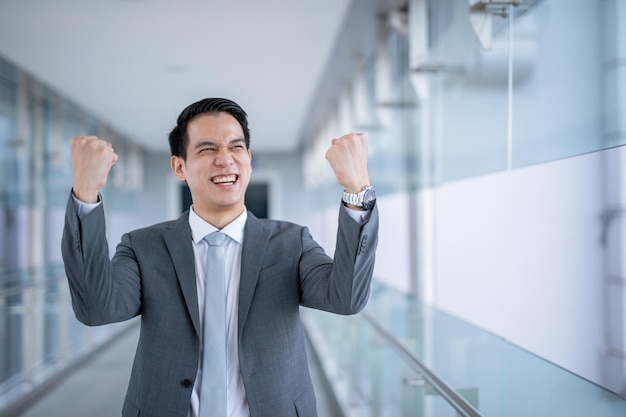 El éxito de un hombre de negocios asiático levanta el puño y celebra la victoria sobre el cargo, un concepto de negocio inteligente.