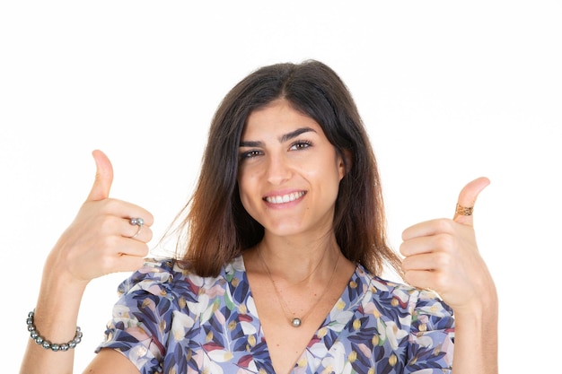 El éxito de una mujer hermosa joven muestra un gesto positivo con los pulgares de los dedos de la mano sonriendo feliz con una expresión alegre en el fondo blanco