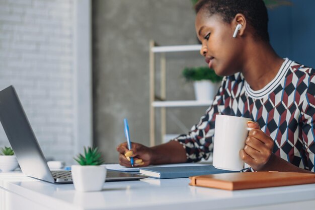 Foto exitosa y atractiva joven empresaria afroamericana sentada en la mesa de la oficina resolviendo problemas matemáticos con libros de texto y dispositivos electrónicos tecnología de negocios corporativos éxito empresarial