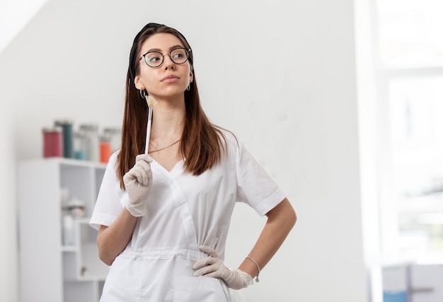 Exitosa doctora cosmetóloga dermatóloga sosteniendo un cepillo en su salón de belleza con ropa médica blanca