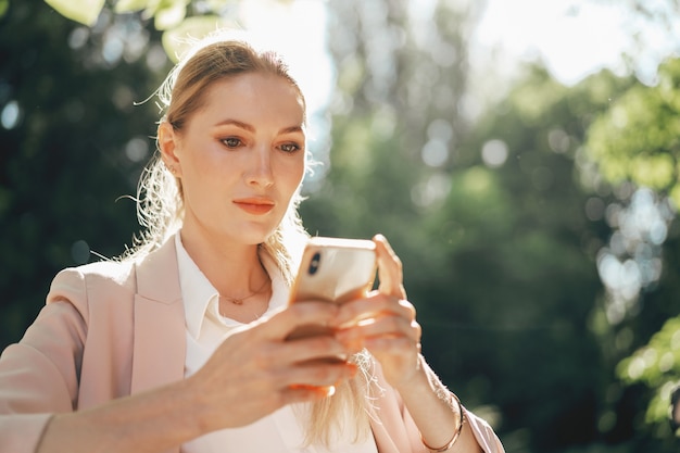 Exitosa empresaria joven sentada en la cafetería al aire libre y con smartphone