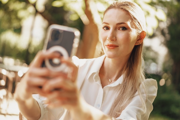 Exitosa empresaria joven sentada en la cafetería al aire libre y con smartphone