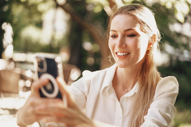 Exitosa empresaria joven sentada en la cafetería al aire libre y con smartphone