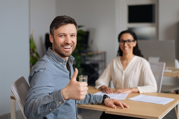 Foto exitosa entrevista de trabajo feliz joven caucásico mostrando gesto de pulgar hacia arriba después de hablar con