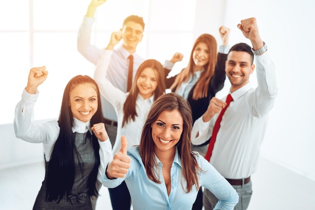 Foto exitosa joven empresaria parada orgullosamente con su joven equipo de negocios. ella está mostrando el pulgar hacia arriba y mirando a la cámara.