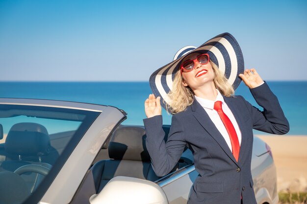 Exitosa joven empresaria en la playa. Mujer de pie cerca del coche clásico descapotable.