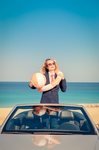 Exitosa joven empresaria en la playa. Mujer de pie en el coche clásico descapotable.