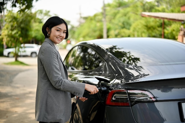 Una exitosa mujer de negocios asiática cargando su auto eléctrico en una estación de carga pública