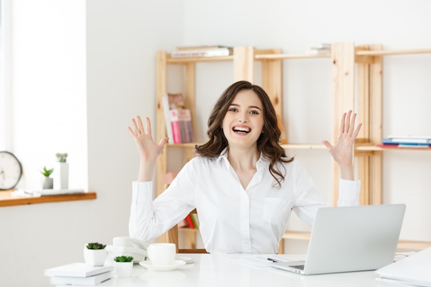 Exitosa mujer de negocios con los brazos arriba sentado en la oficina moderna.