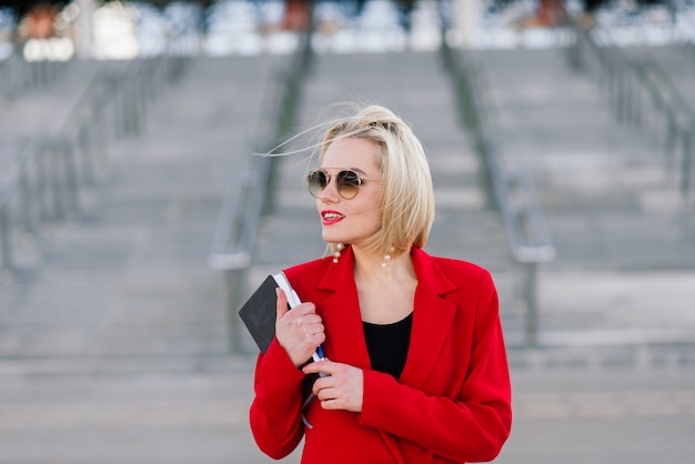 Exitosa mujer de negocios en capa roja hablando por teléfono inteligente negociando un acuerdo en el fondo de altos edificios en el centro de negocios.