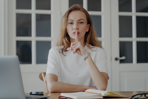 Exitosa mujer de negocios de mediana edad está trabajando desde casa y hace gestos de silencio Concepto de secreto