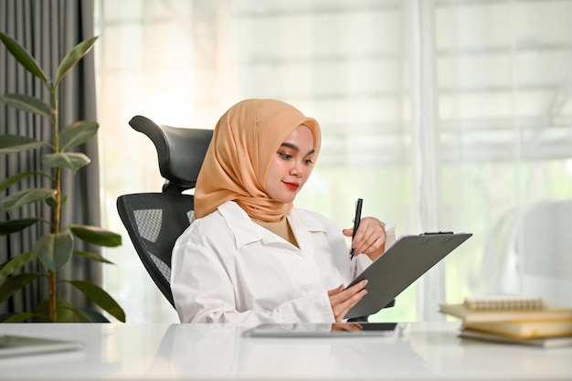 Exitosa mujer de negocios musulmana asiática leyendo y revisando informes de negocios en su oficina