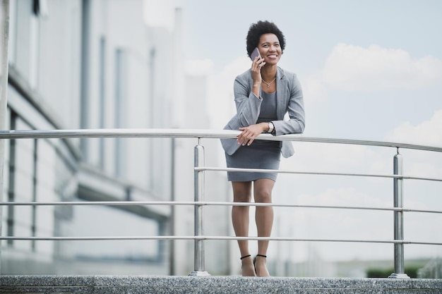 Una exitosa mujer de negocios negra que usa un teléfono inteligente frente a un edificio corporativo.