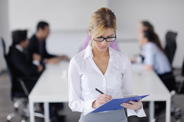 Exitosa mujer de negocios de pie con su personal en segundo plano en una oficina moderna y luminosa