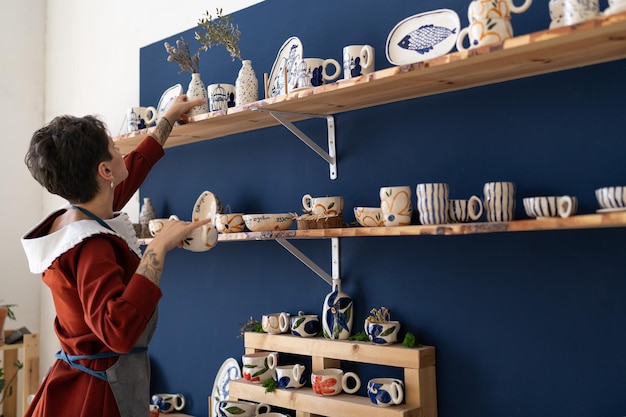 Exitosa mujer propietaria de una tienda de vajillas decora el interior con jarrones de porcelana con plantas secas