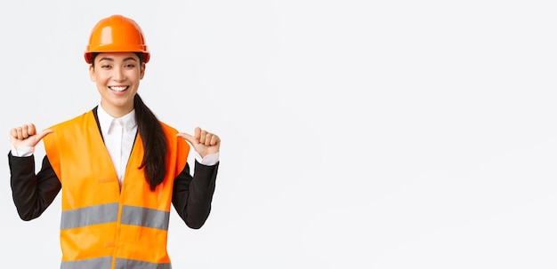 Exitosa, orgullosa y sonriente ingeniera asiática gerente de construcción con casco de seguridad apuntándola