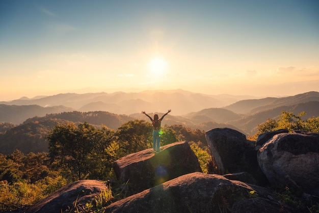 Exitosa silueta joven excursionista de pie en la cima del pico de la montaña al atardecer en el parque nacional