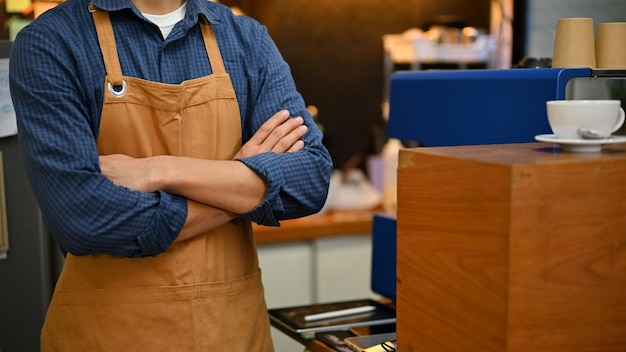 Exitoso barista masculino asiático en delantal con los brazos cruzados en la cafetería