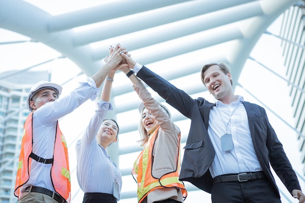 Exitoso grupo de empresarios e ingenieros con unir sus manos al aire libre en la ciudad. Haciendo negocios junto a un grupo de ingenieros y empresarios. Dos ingenieros y dos empresarios.