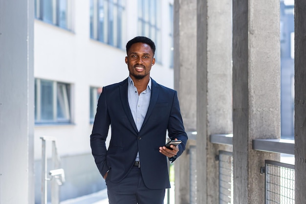 Exitoso hombre de negocios afroamericano sonríe y mira a la cámara, feliz usa el teléfono y mantiene los pulgares arriba