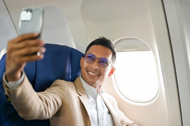 Foto exitoso hombre de negocios asiático tomando su foto con un smartphone durante el vuelo