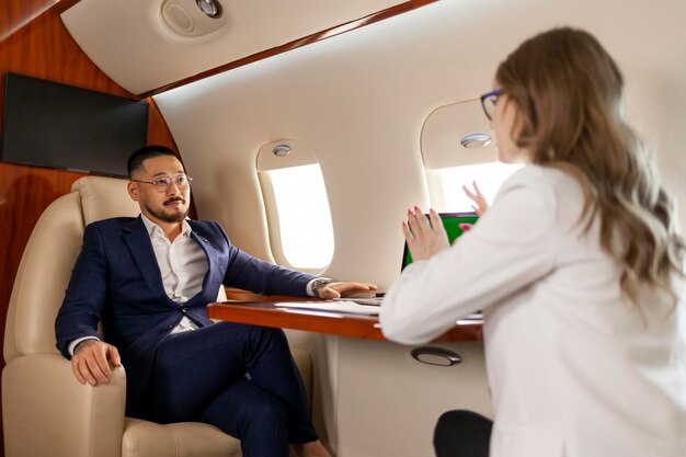 Un exitoso hombre de negocios asiático en traje se reúne con una mujer de negocios en un avión privado.