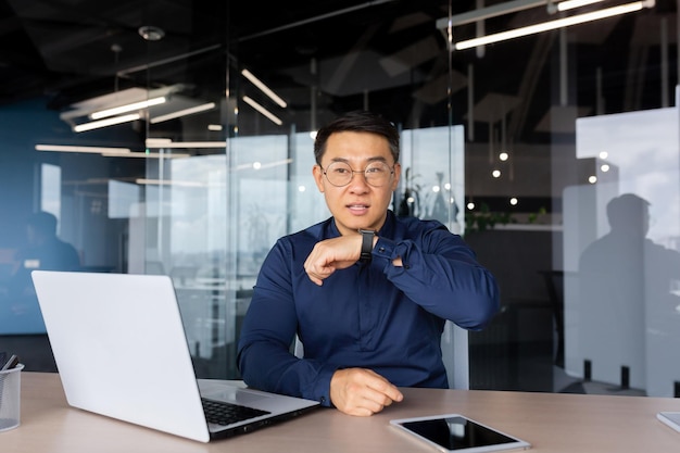 Exitoso hombre de negocios dentro de la oficina usando la aplicación en un reloj inteligente para comunicar al hombre asiático dando voz
