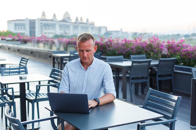 Exitoso hombre de negocios joven que trabaja con una laptop de vacaciones. Lleva una camiseta y pantalones cortos blancos. Trabajo fuera de la oficina, autónomo