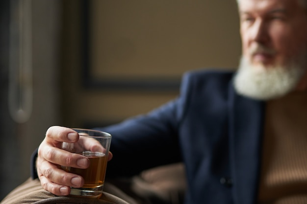 Exitoso hombre de negocios de mediana edad sosteniendo un vaso de whisky escocés de alcohol en la mano mientras