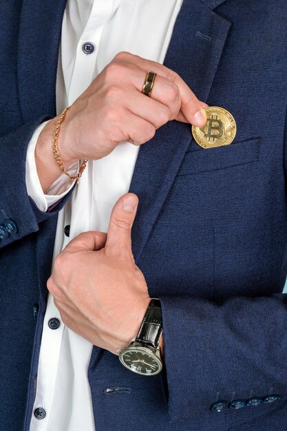 Un exitoso hombre de negocios pone una moneda de oro bitcoin en el bolsillo del pecho de su chaqueta cerrada