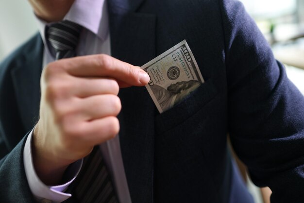 Un exitoso hombre de negocios saca un billete de un dólar del bolsillo del pecho de un hombre de traje clásico listo para