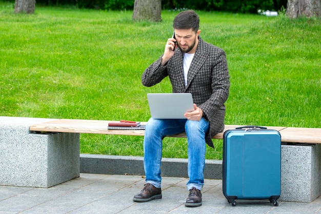 Un exitoso hombre de negocios se sienta en un banco de la ciudad y se dedica a hacer negocios con documentos y una computadora portátil