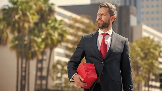 Exitoso hombre de negocios en traje mantenga caja presente aniversario al aire libre permanente