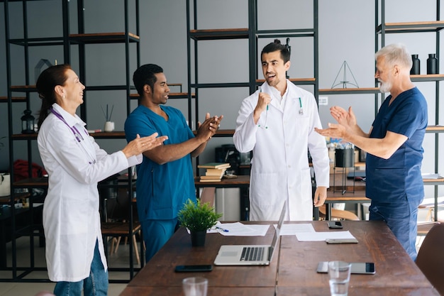 Exitoso médico joven y calificado que recibe el aplauso del equipo en la sala de la oficina en un hospital moderno Grupo de médicos multiétnicos que aplauden para agradecerle al equipo médico Concepto de medicina y atención médica