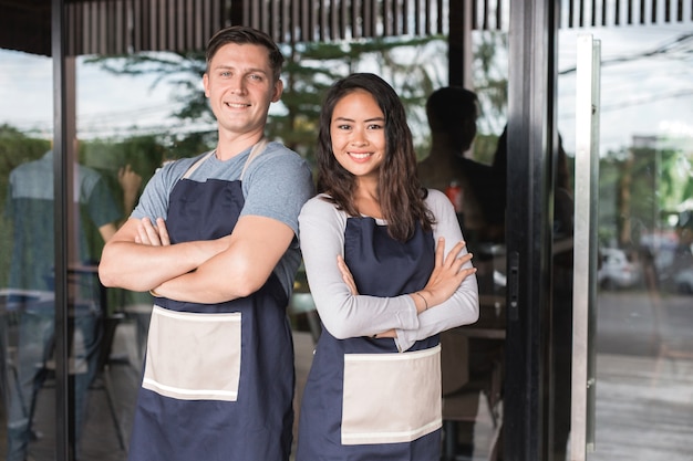 Exitoso propietario de una pequeña empresa masculina y femenina de pie con orgullo frente a su cafetería o cafetería