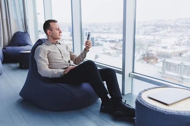 Exitoso trabajador independiente masculino sentado en un espacio de trabajo moderno y revisando notificaciones en teléfonos móviles con ropa informal Trabajo remoto