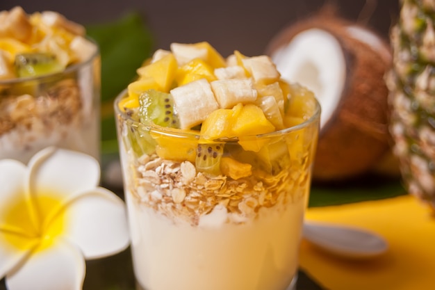 Exótica ensalada de frutas tropicales con muesli y yogurt en un vaso con piña y coco en el fondo.