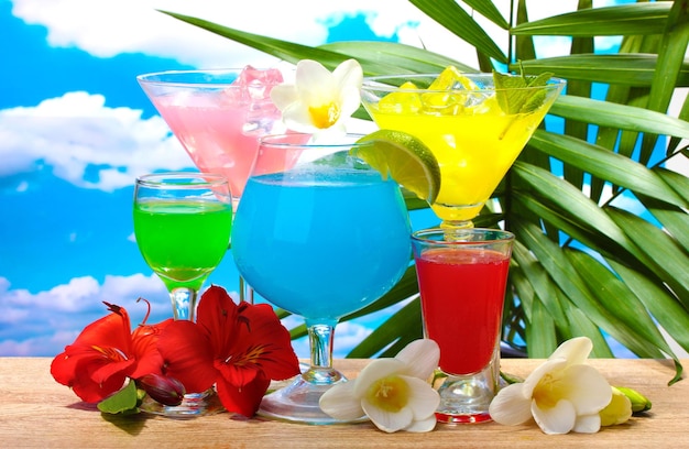 Foto exotische cocktails und blumen auf dem tisch auf blauem himmelshintergrund