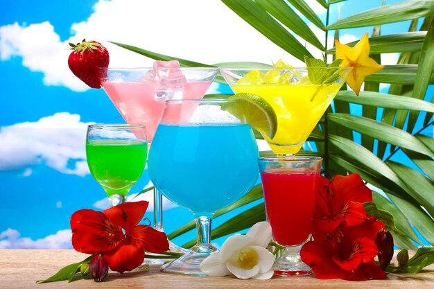 Exotische Cocktails und Blumen auf dem Tisch auf blauem Himmelshintergrund