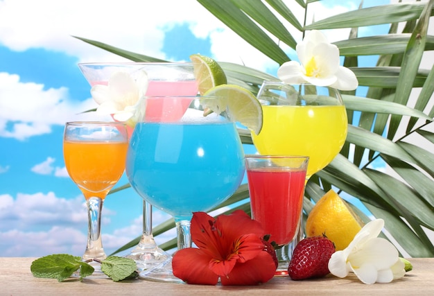 Exotische Cocktails und Blumen auf dem Tisch auf blauem Himmelshintergrund