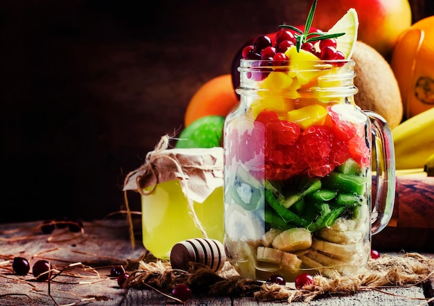 Exotischer Obstsalat mit Bananen-Kiwi-Grapefruit-Mango-Cranberry- und Zitronensaft und Honig, serviert in einem Glas Vintage-Holzhintergrund, selektiver Fokus