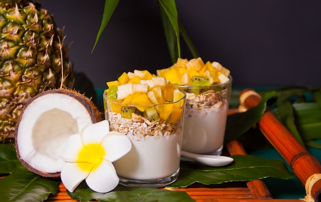 Exotischer tropischer Obstsalat mit Müsli und Joghurt in einem Glas auf dem Palmblatt.