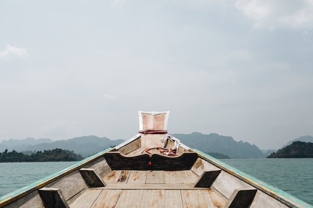 Exotisches Holzboot mit tropischen Inseln mit Felsen und blauem See am Cheow Lan See, Khao Phang, Ban Ta Khun Bezirk