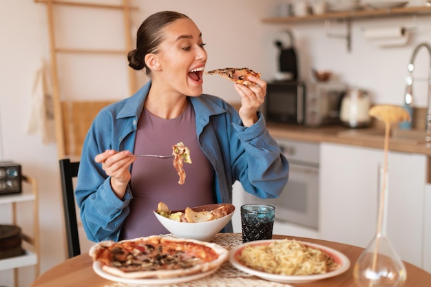 Foto expectante delicias hambrienta mujer embarazada comiendo pizza y ensalada teniendo deseo de comida chatarra sentada